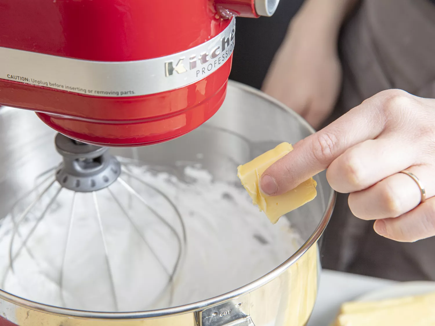 Closeup of a hand dropping a cube of butter into a stand mixer full of sugar to make buttercream